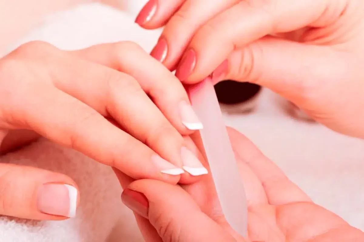Lima profesional dando forma a uñas durante sesión de manicura con tonos rosados
